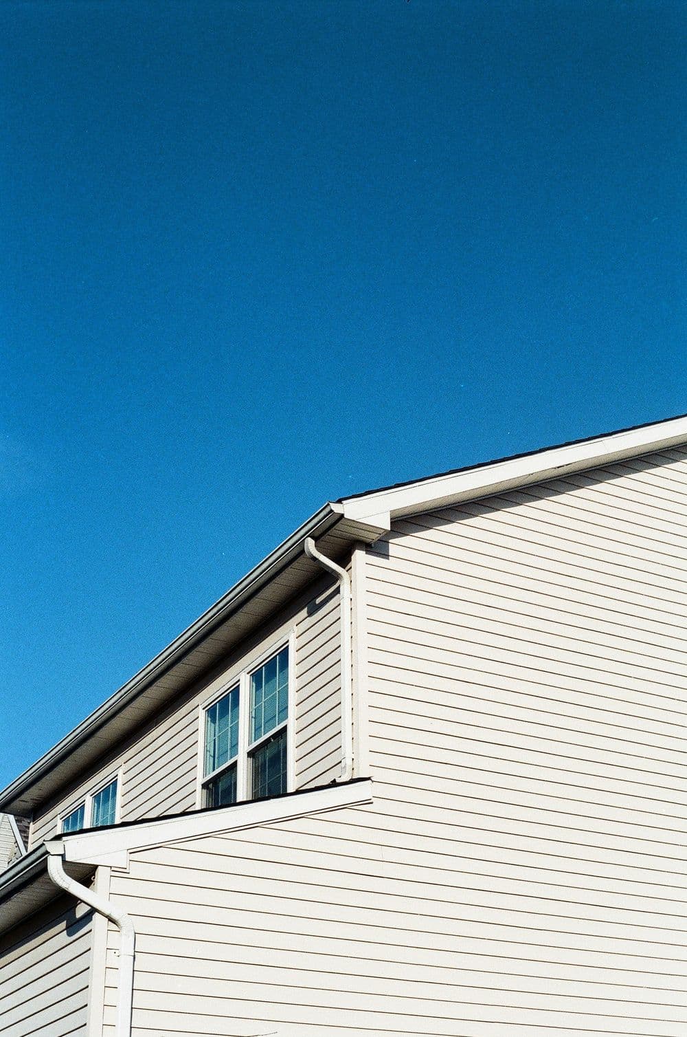 Light-colored house exterior against a clear blue sky, showcasing architectural details.