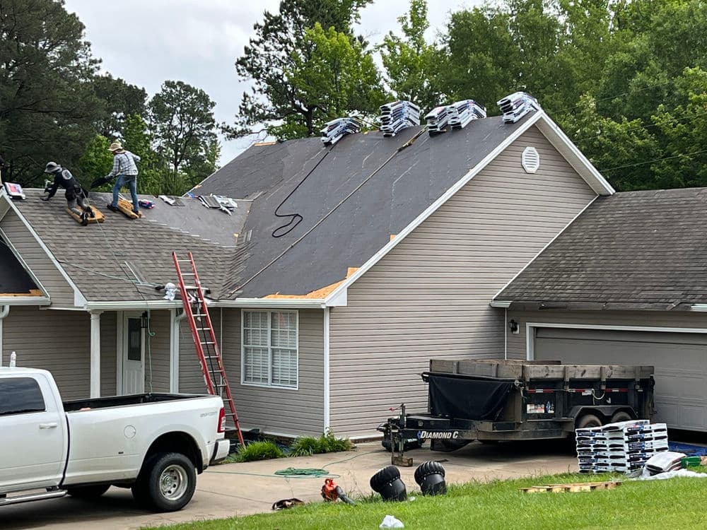 Roofers installing new shingles on a residential roof with tools and materials nearby.
