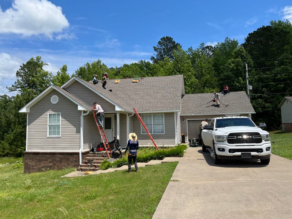 Roofing crew working on a house with a white truck parked in the driveway on a sunny day.